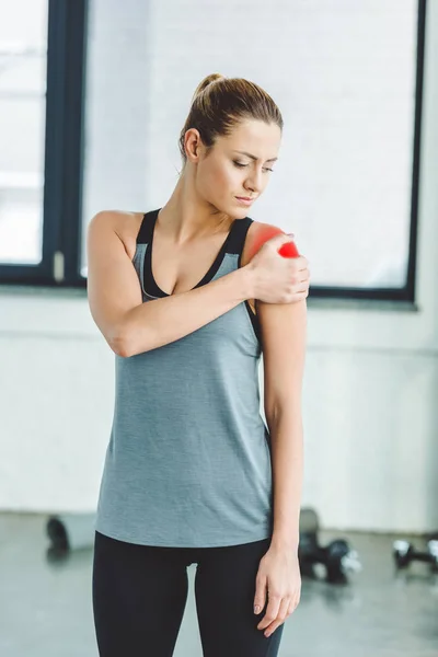 Portrait of young sportswoman suffering from pain in arm at gym — Stock Photo