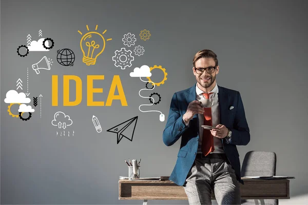 Sonriente hombre de negocios con taza de café sentado en la mesa y mirando a la cámara, concepto de la idea - foto de stock