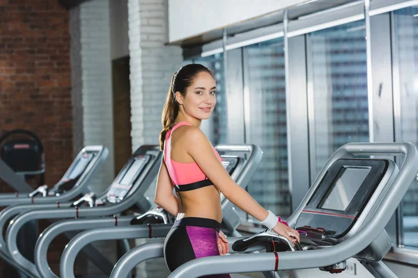 Mujer deportiva de pie en la cinta y mirando a la cámara - foto de stock