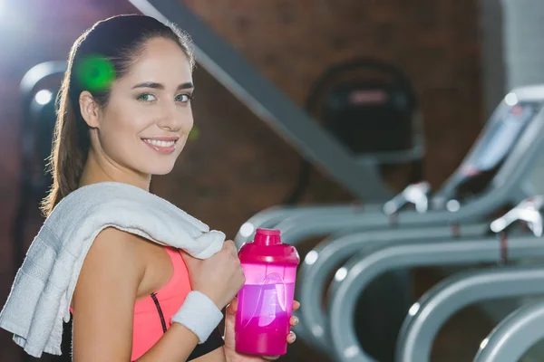 Sporty woman standing with shaker and towel in hands against treadmills — Stock Photo