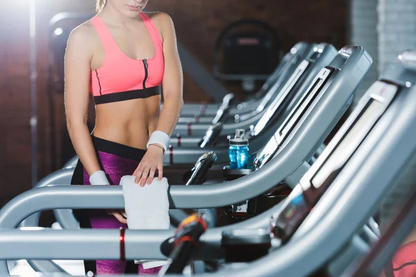 Cropped image of sporty woman standing on treadmill and touching towel — Stock Photo