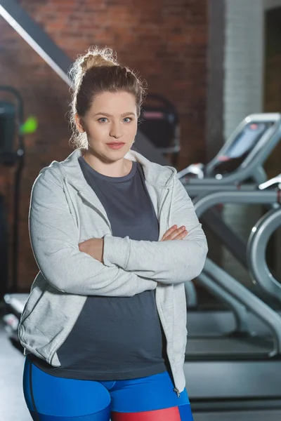 Overweight woman standing at gym with arms crossed and looking at camera — Stock Photo