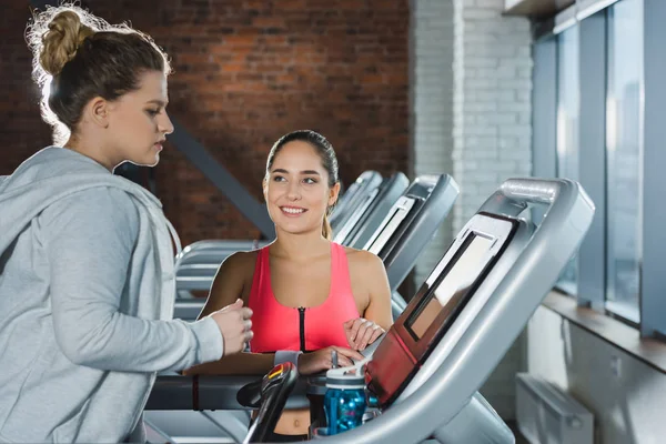 Übergewichtige Frau trainiert auf Laufband, während Trainer sie beobachtet — Stockfoto