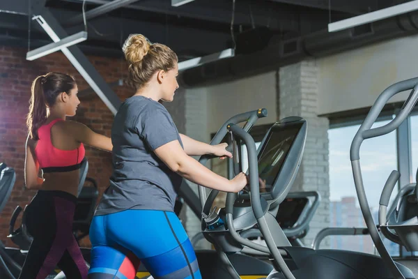 Спортивные и толстые женщины тренируются на беговых дорожках в тренажерном зале — стоковое фото