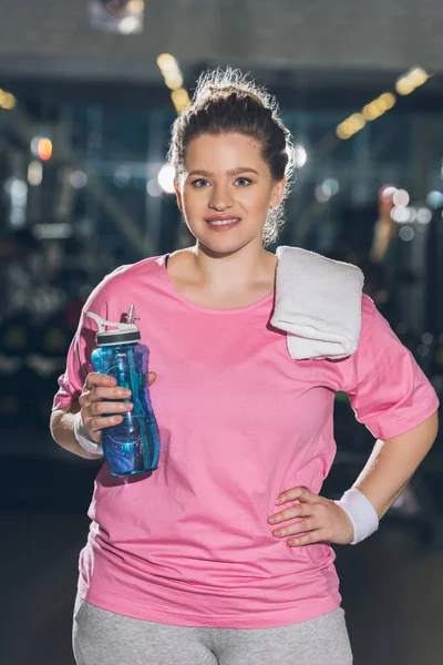 Übergewichtige Frau steht mit Handtuch und Wasserflasche vor der Kamera — Stockfoto