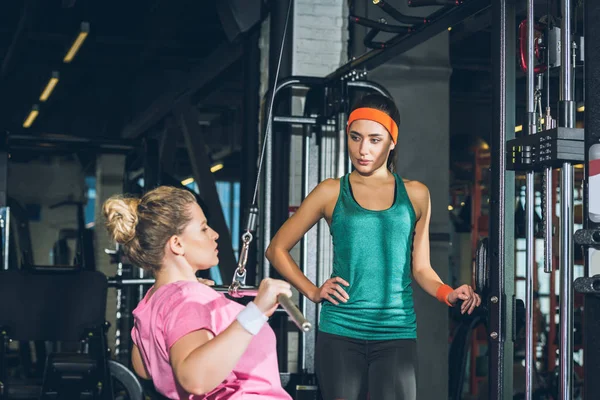 Donna in sovrappeso che lavora su un apparecchio di formazione mentre l'allenatore la guarda — Foto stock