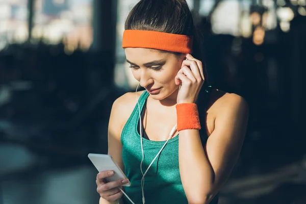 Sportliche Frau nutzt Smartphone und Kopfhörer im Fitnessstudio — Stockfoto