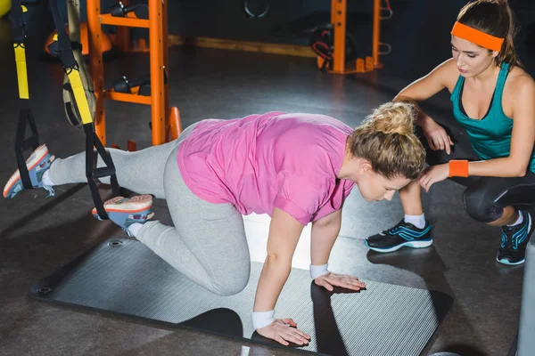 Übergewichtige Frau trainiert an Aufhängebändern, während der Trainer sie beobachtet — Stockfoto