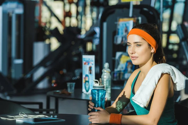 Sportliche Frau sitzt mit Wasserflasche am Tisch im Fitnessstudio — Stockfoto