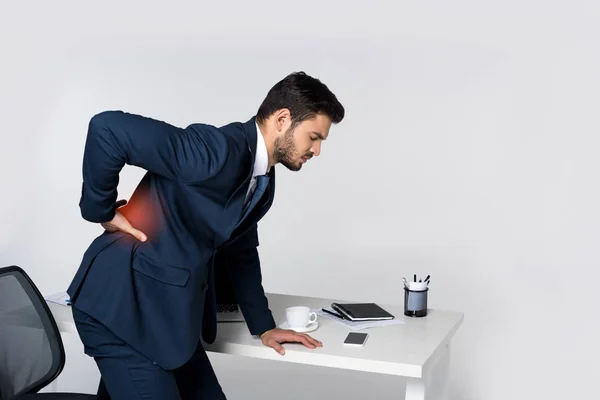 Seitenansicht eines jungen Geschäftsmannes, der unter Rückenschmerzen leidet und sich am Bürotisch lehnt — Stockfoto