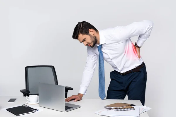 Jeune homme d'affaires souffrant de maux de dos tout en se penchant à la table avec ordinateur portable — Photo de stock