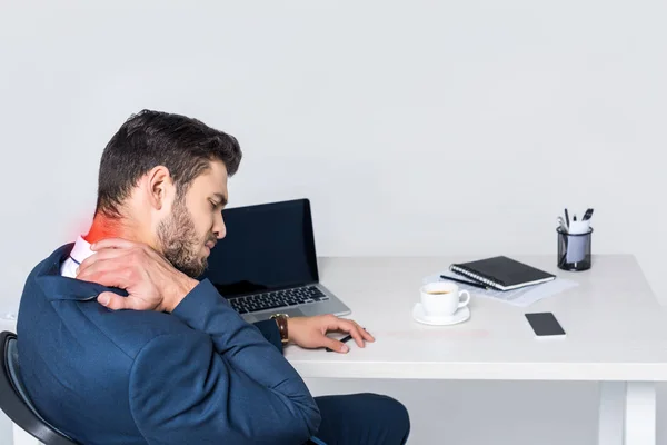 Young businessman suffering from pain in neck while sitting at workplace — Stock Photo
