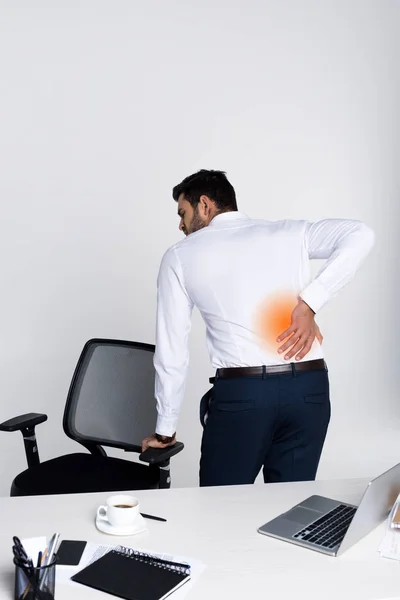 Young businessman suffering from backache while leaning at chair in office — Stock Photo