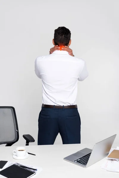 Вид сзади молодого бизнесмена, страдающего от боли в шее, стоя на рабочем месте — стоковое фото