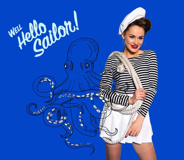 Smiling beautiful young woman in sailor shirt with rope, octopus drawing and well hello sailor inscription isolated on blue — Stock Photo