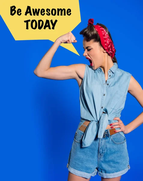 Mujer joven en ropa retro mostrando los músculos y gritando con ser impresionante hoy burbuja de habla aislado en azul - foto de stock