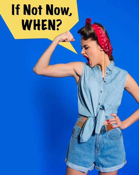 Mujer joven con ropa retro mostrando músculos y gritando con SI NO AHORA, CUANDO? burbuja de habla aislada en azul - foto de stock