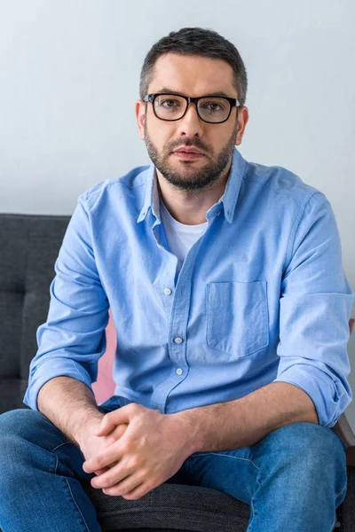 Portrait of man in eyeglasses sitting on sofa and looking at camera — Stock Photo