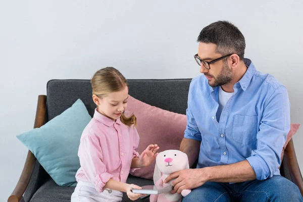 Retrato de padre jugando con hija con juguete en sofá en casa - foto de stock