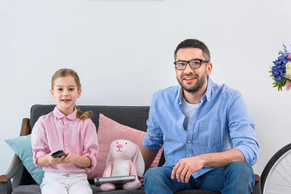 Улыбающаяся семья отдыхает на диване и смотрит телевизор дома — стоковое фото