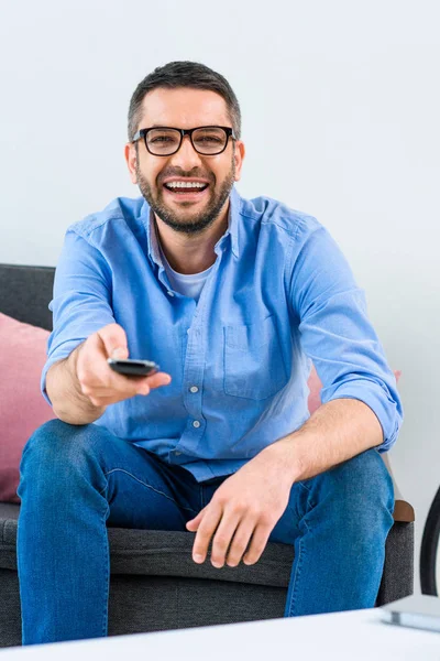 Porträt eines fröhlichen Mannes, der die Kanäle wechselt, während er zu Hause fernsieht — Stockfoto