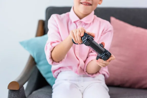 Vista parcial de niño con gamepad en las manos jugando videojuego en casa - foto de stock