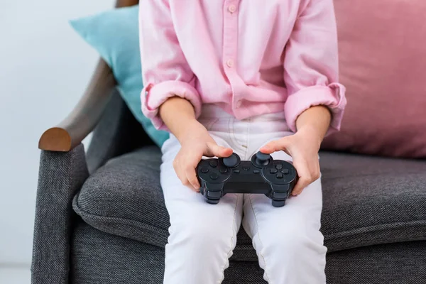 Partial view of kid with gamepad in hands playing video game at home — Stock Photo