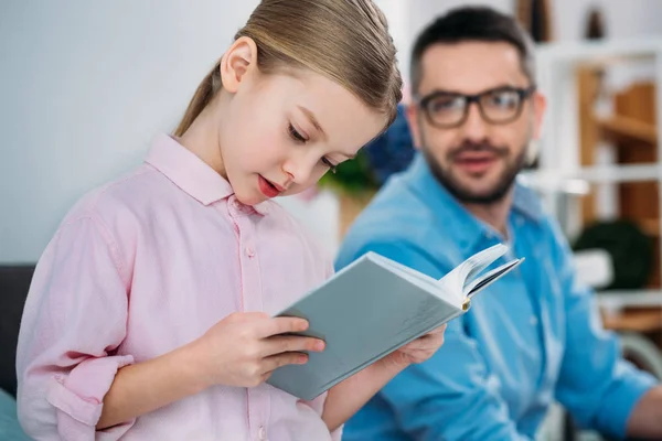 Messa a fuoco selettiva del padre guardando figlia lettura libro — Stock Photo