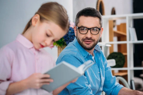 Selective focus of father looking at daughter reading book — Stock Photo