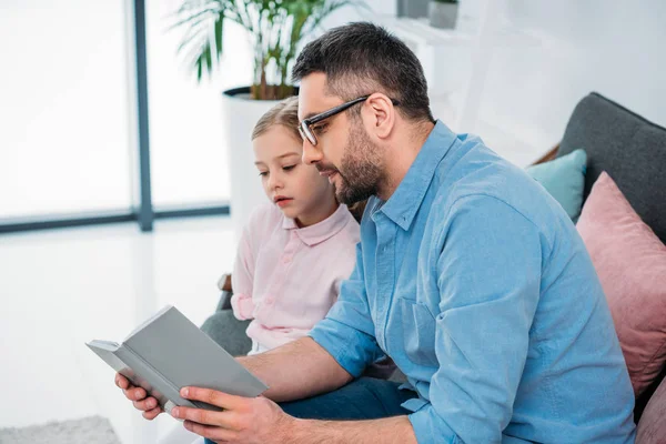 Вид збоку батька і дочки читають книгу вдома — Stock Photo