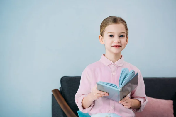 Портрет чарівної маленької дитини з книгою, що сидить на дивані вдома — стокове фото