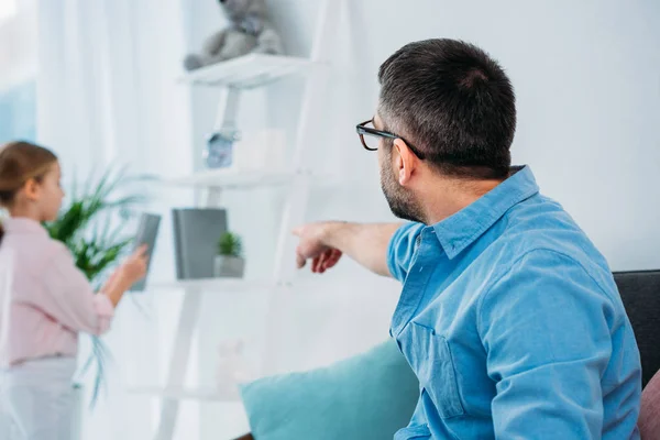 Vater zeigt selektiv auf Buch im Regal für Tochter zu Hause — Stockfoto