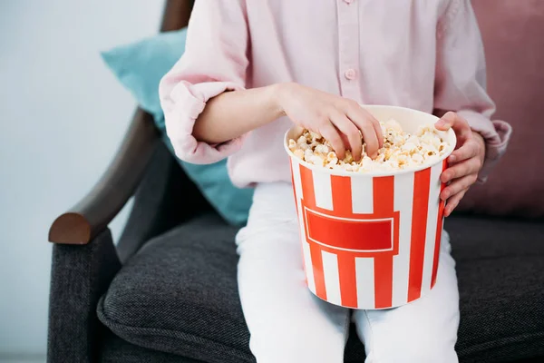 Cropped shot of kid with popcorn sitting on sofa at home — Stock Photo