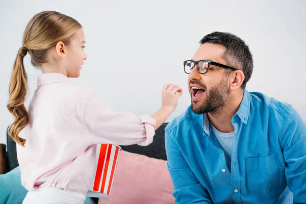 Vue latérale de l'enfant nourrissant père avec pop-corn à la maison — Photo de stock