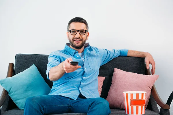 Человек в очках отдыхает на диване и смотрит телевизор дома — стоковое фото