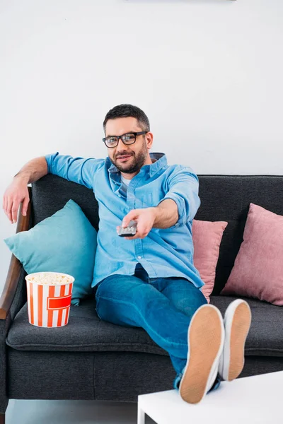 Homme aux lunettes reposant sur le canapé et regardant la télévision à la maison — Photo de stock