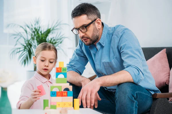 Portrait of family building pyramid from colorful blocks at home — Stock Photo