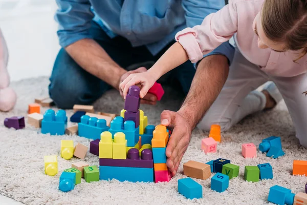 Cropped shot of daughter and father playing with colorful blocks together on floor at home — Stock Photo