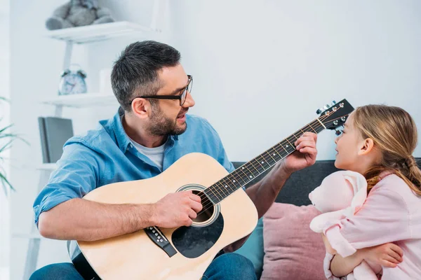 Man playing acoustic guitar for daughter in living room — Stock Photo