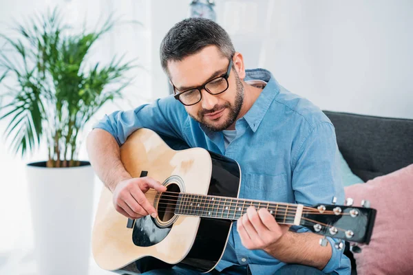 Retrato de homem em óculos tocando guitarra acústica em casa — Fotografia de Stock