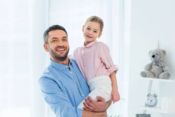 Retrato de padre feliz sosteniendo a la pequeña hija en las manos en casa - foto de stock