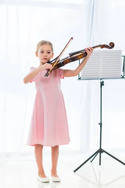 Mignon petit enfant en robe rose jouant du violon à la maison — Photo de stock