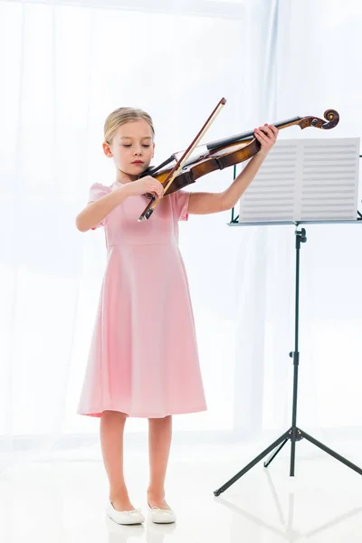 Mignon petit enfant en robe rose jouant du violon à la maison — Photo de stock