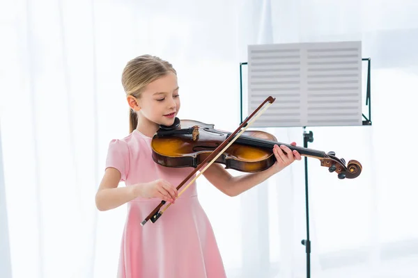 Petit enfant souriant en robe rose jouant du violon à la maison — Photo de stock