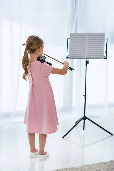 Vue arrière du petit enfant en robe rose jouant du violon à la maison — Photo de stock