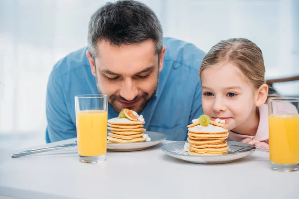 Portrait of father and little daughter sniffing pancakes for breakfast at home — Stock Photo