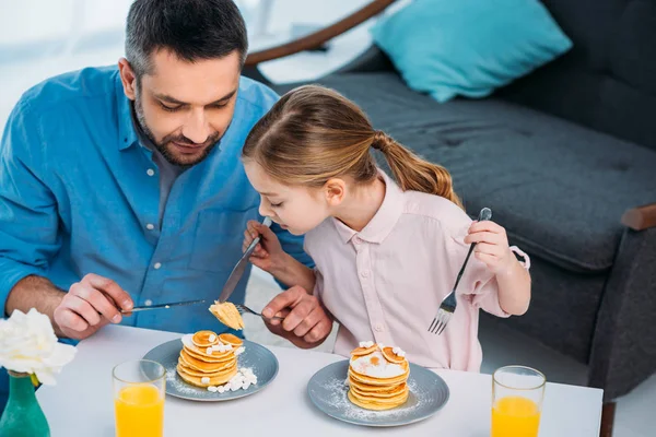 Padre e hija pequeña desayunando en casa - foto de stock
