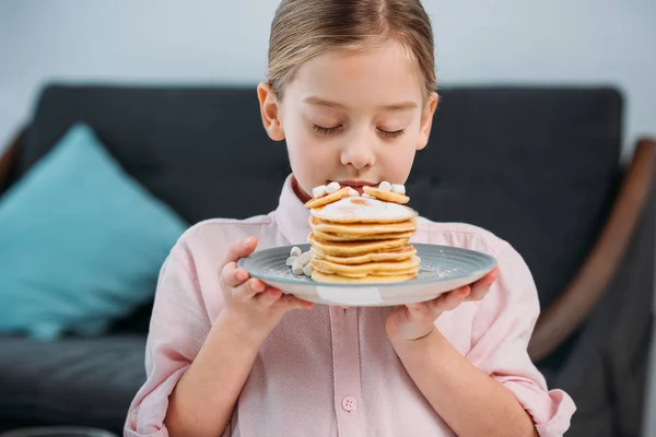 Retrato de criança cheirando panquecas caseiras na placa para o café da manhã em mãos — Fotografia de Stock