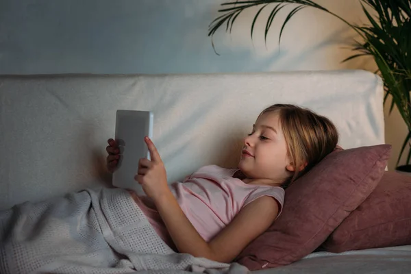 Vue latérale du petit enfant en utilisant une tablette au lit à la maison — Photo de stock