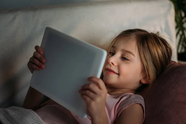 Vista lateral del niño pequeño usando la tableta en la cama en casa - foto de stock